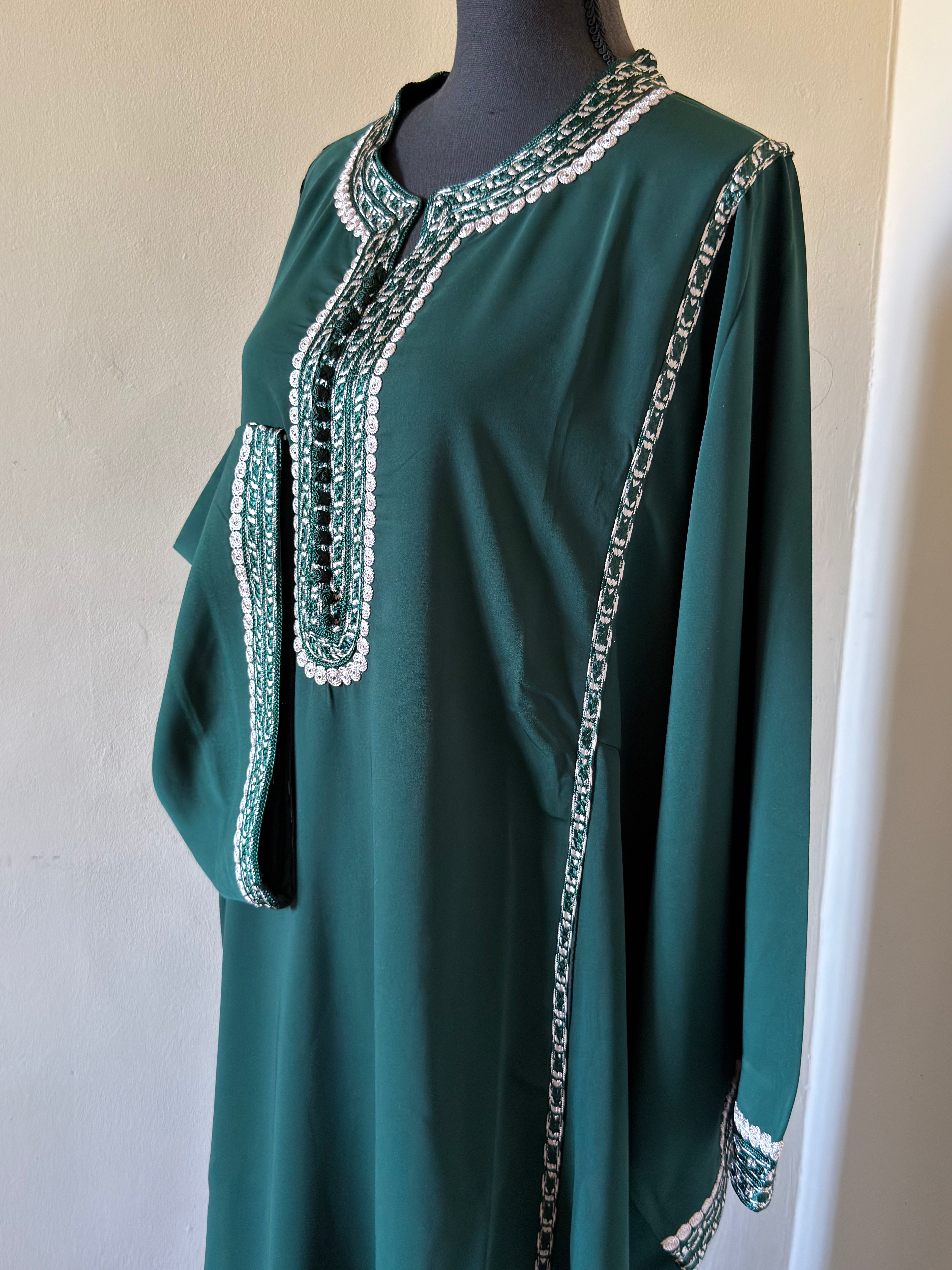Green dress with intricate white embroidery on a mannequin against a plain background