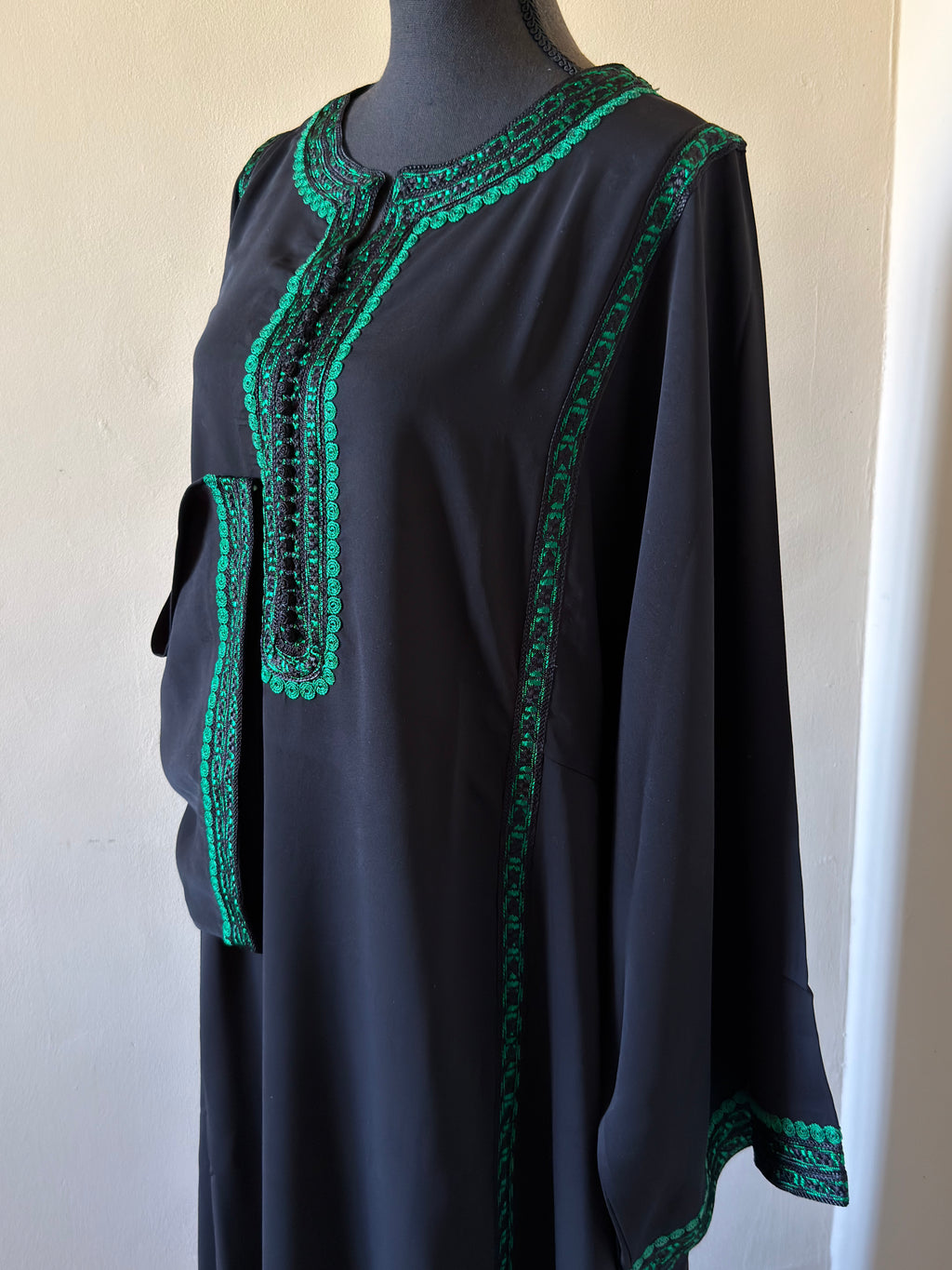 Black dress with green embroidery on a mannequin against a white background