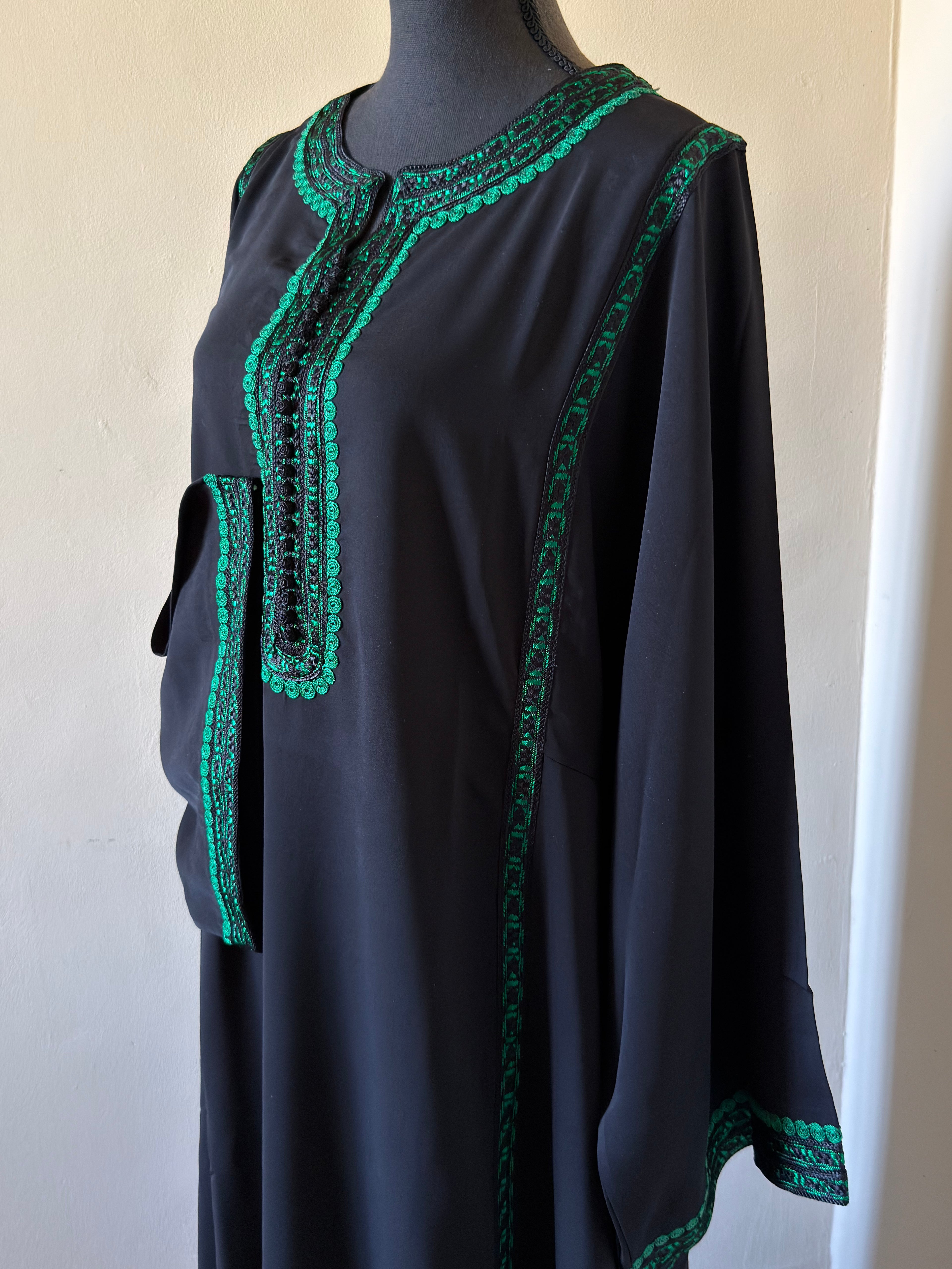 Black dress with green embroidery on a mannequin against a white background
