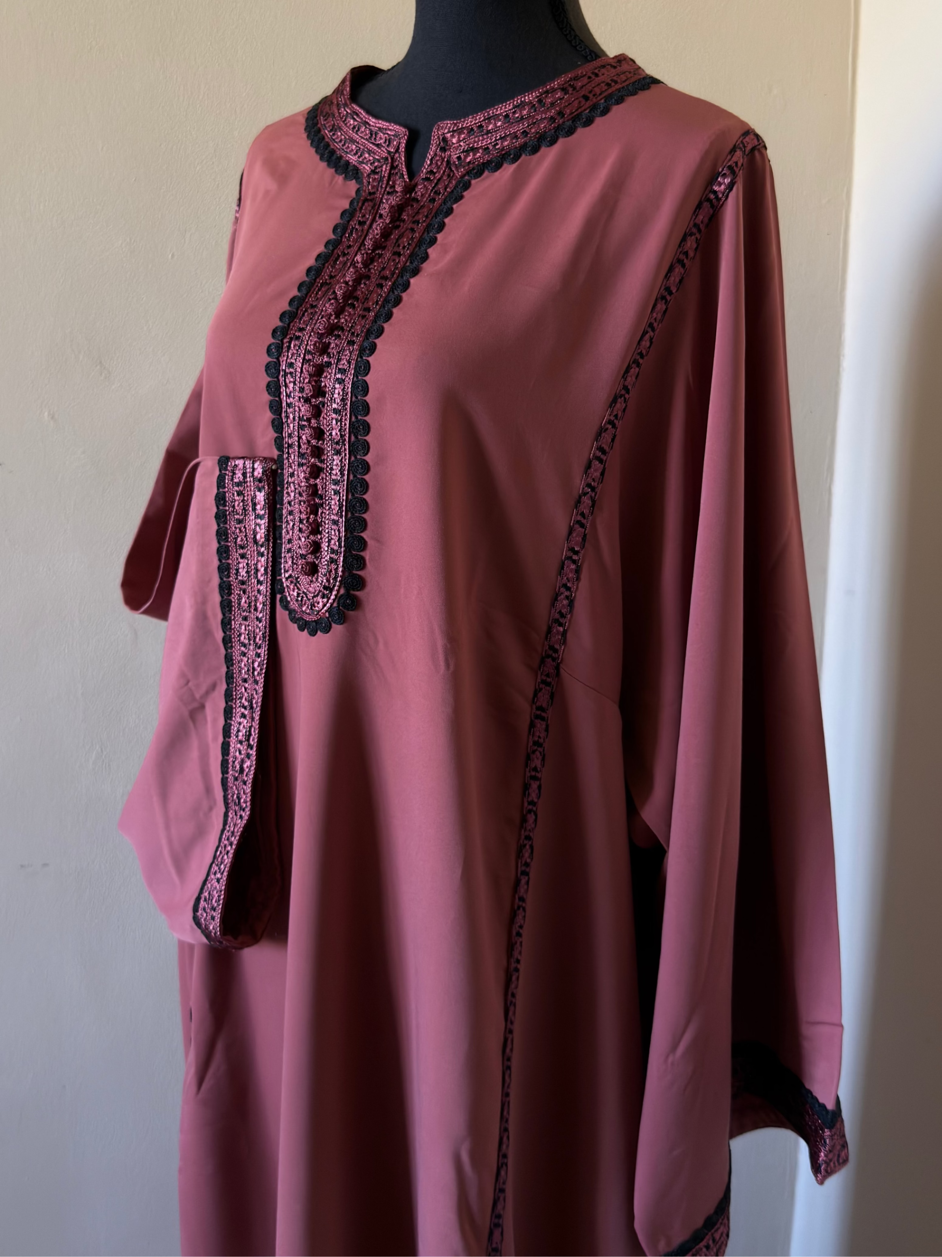 Pink dress with black embroidery on a mannequin against a plain background