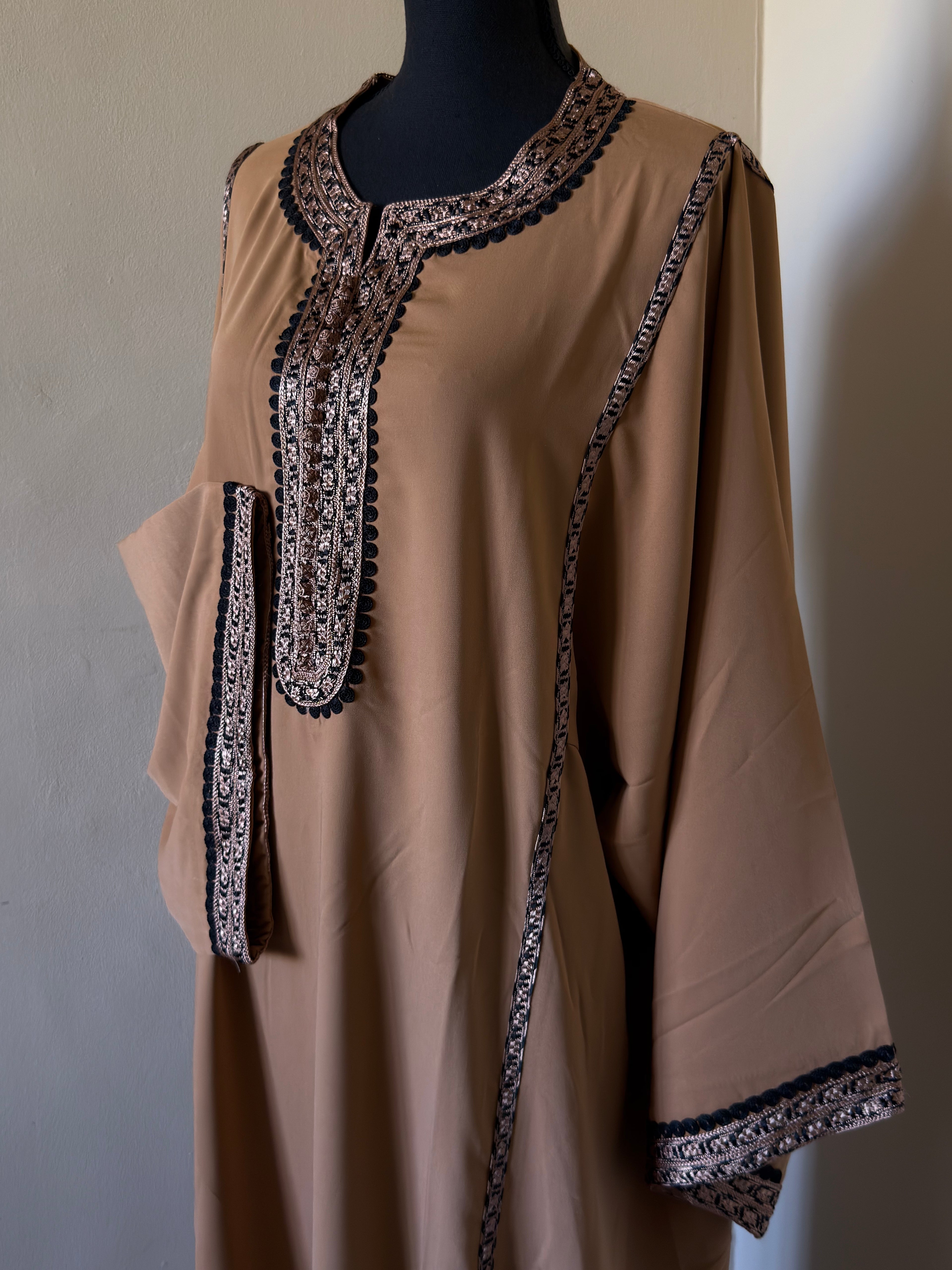 Beige dress with intricate black and white embroidery on a mannequin against a plain background