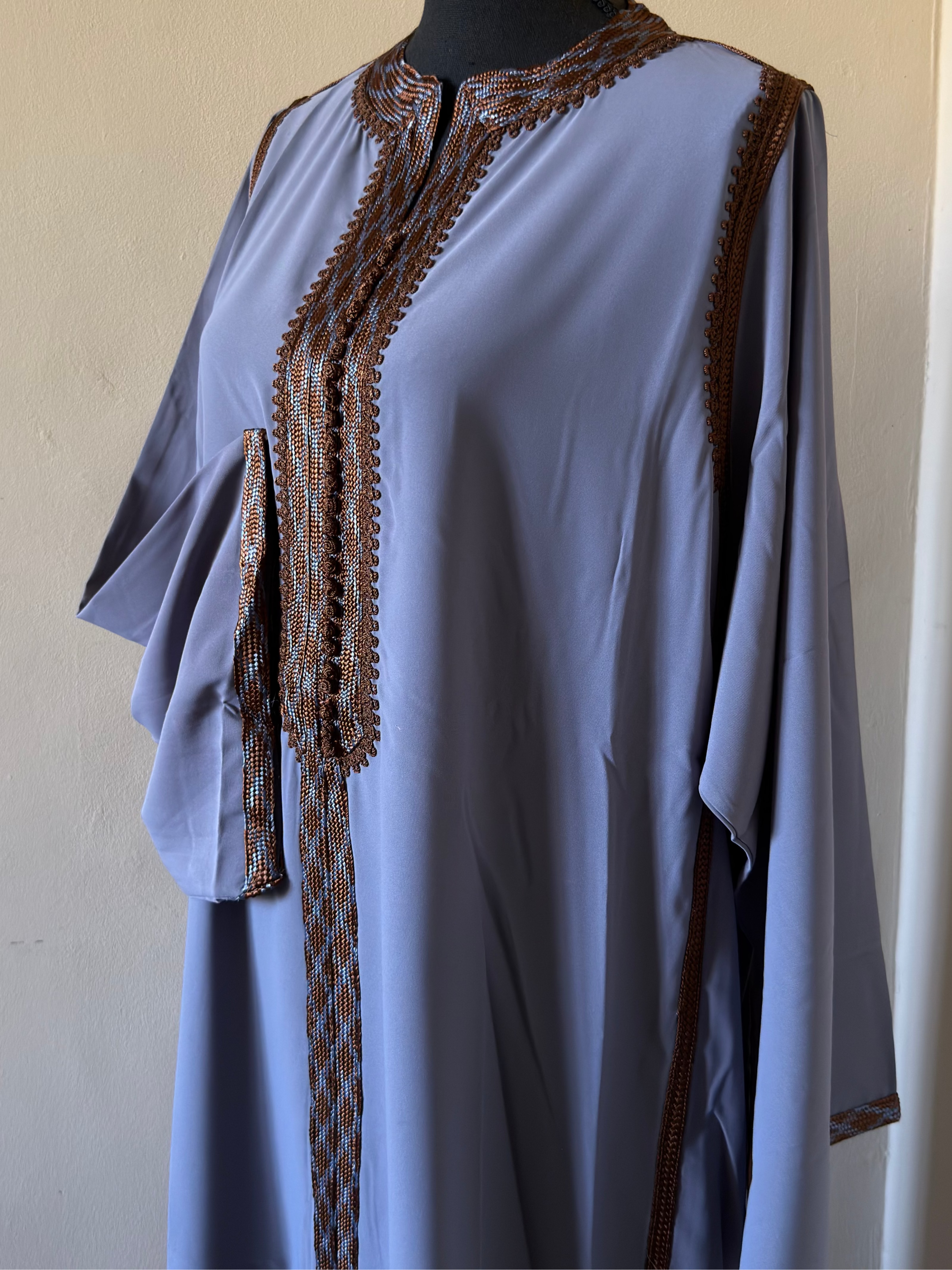 Light blue dress with brown embroidery on a mannequin against a beige wall.