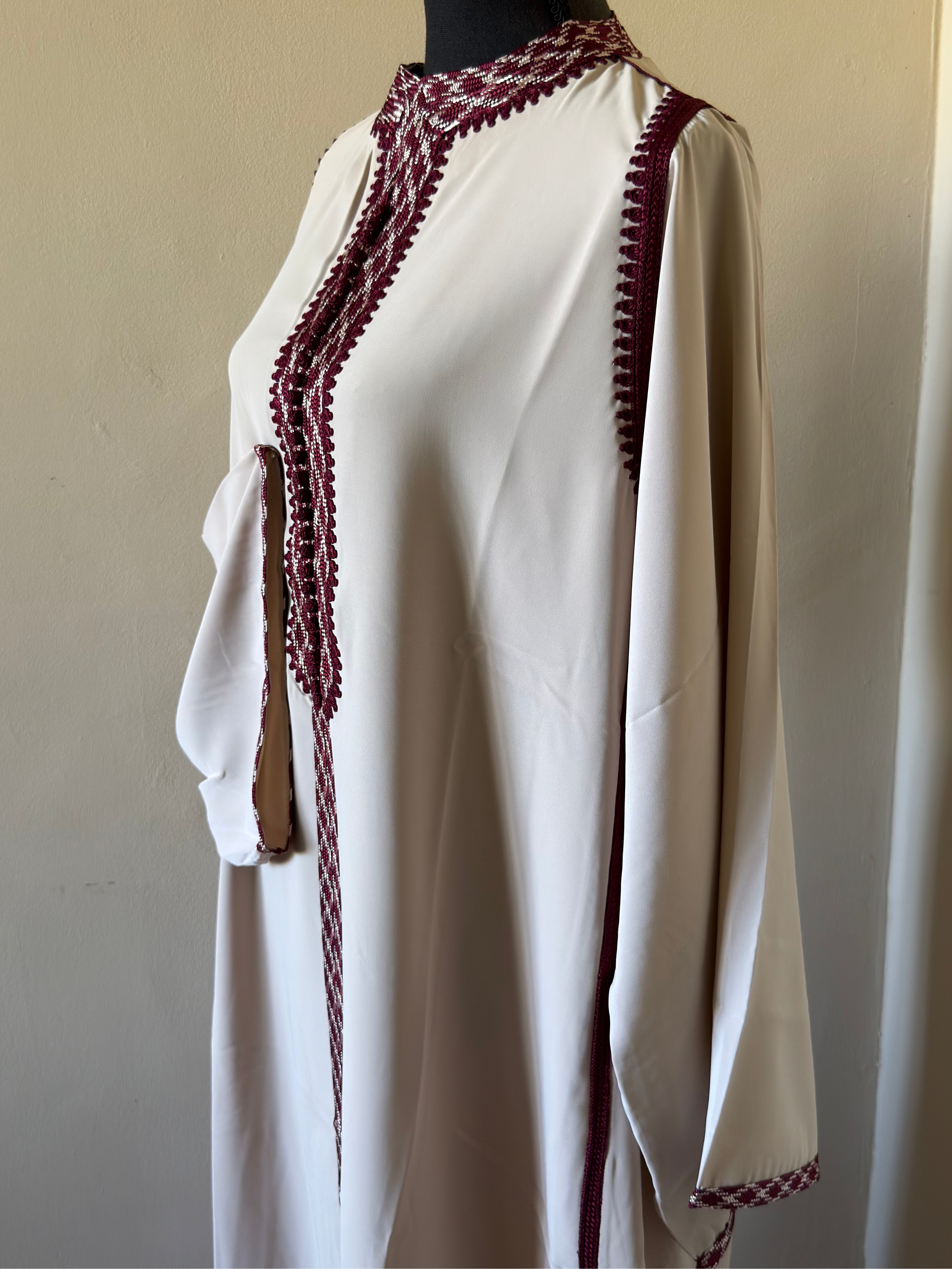White dress with red lace details on a mannequin against a plain background
