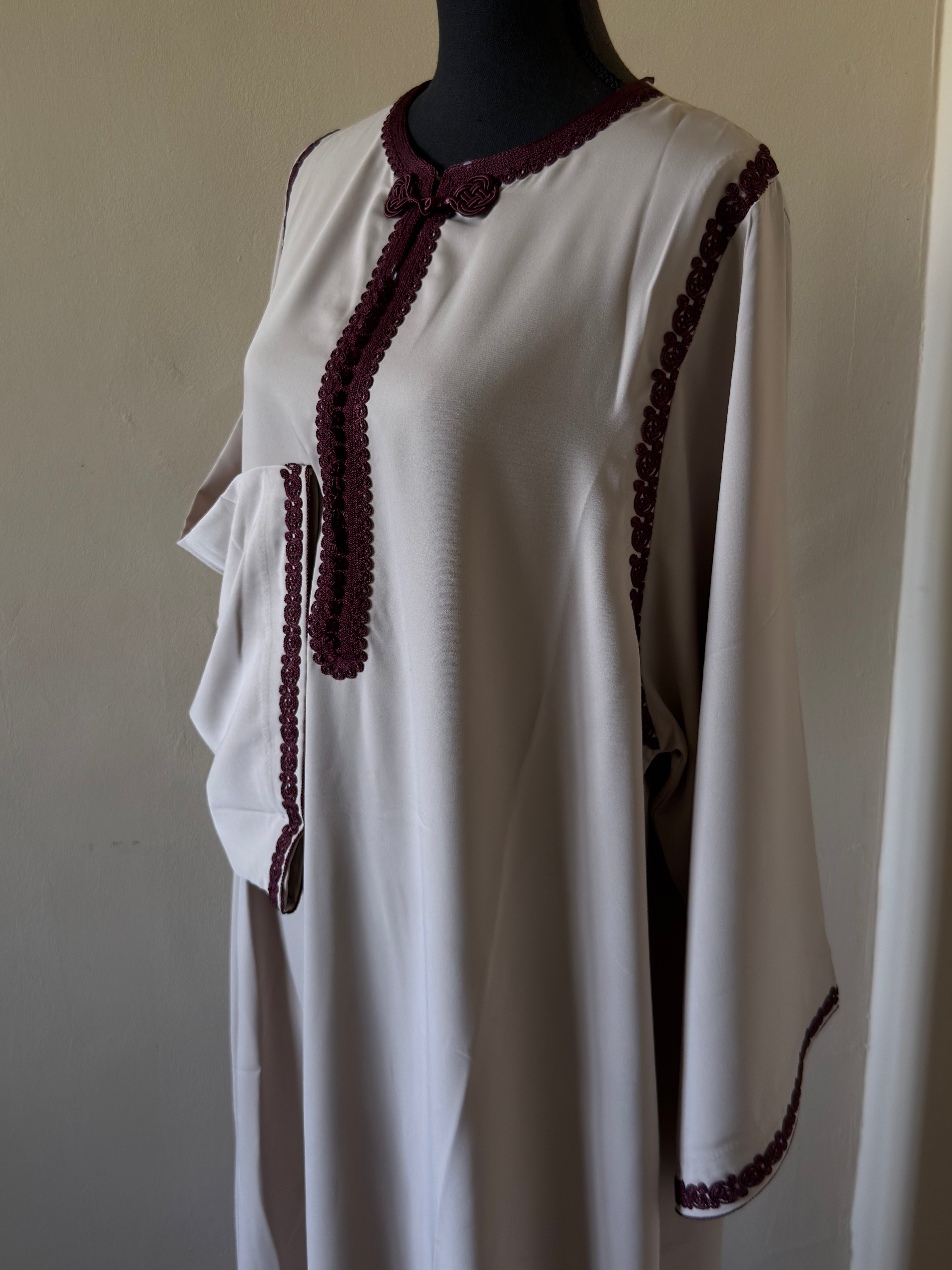 White dress with maroon trim on a mannequin against a plain background